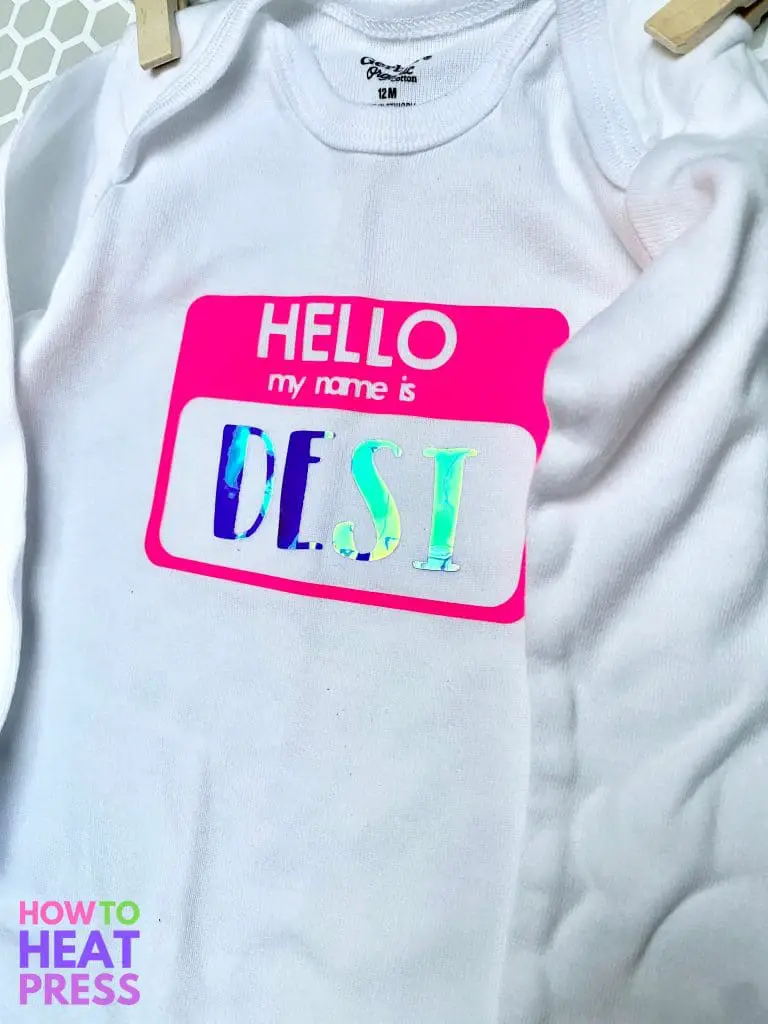 white cricut baby onesie with neon pink name tag and holographic blue htv