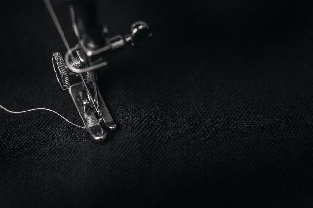 black fabric, presser foot, and white thread of sewing machine