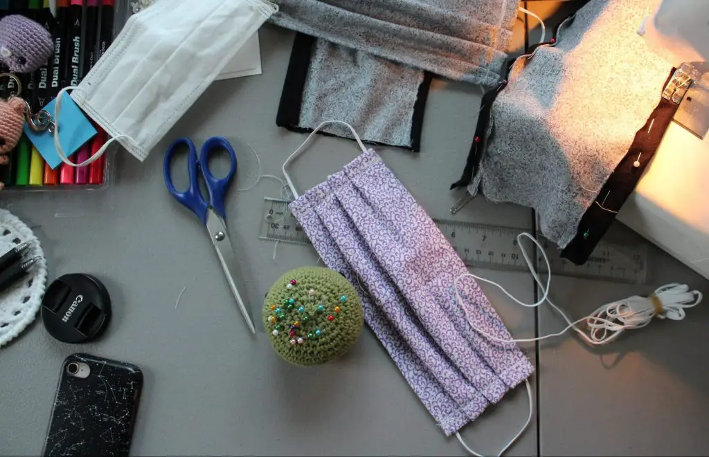 sewing machine, fabric, and scissors in work area making masks